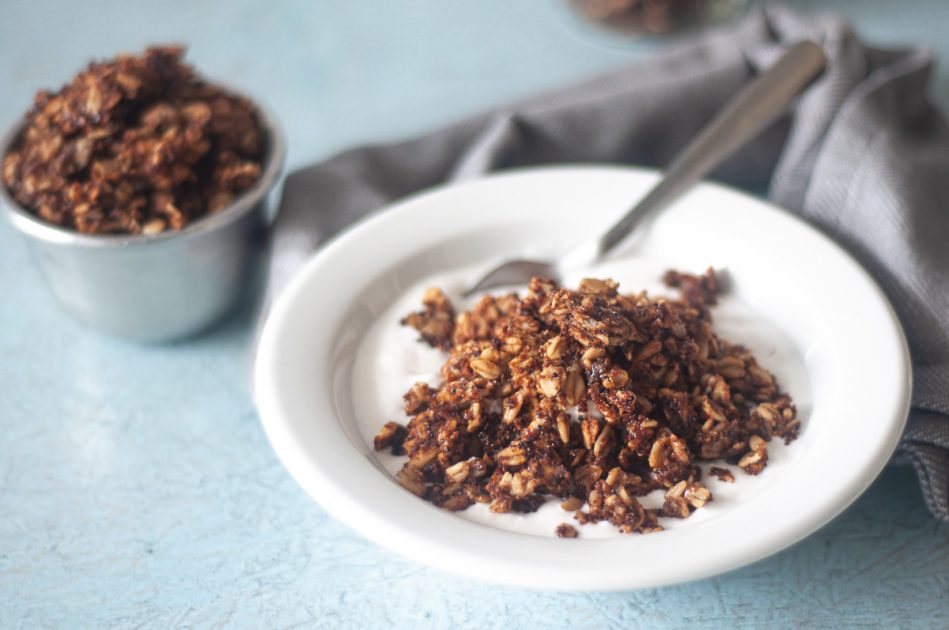 A white bowl of kaniwa granola and coconut milk, with a spoon.