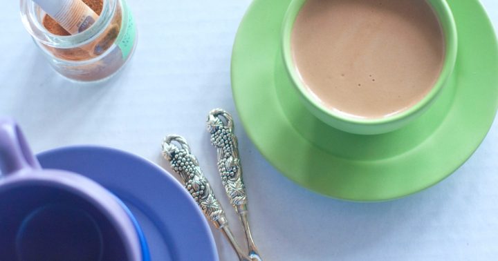 An overhead shot of a green coffee coffee cup with pumpkin spice coffee, a small jar of the spice blend and an empty blue coffee cup.