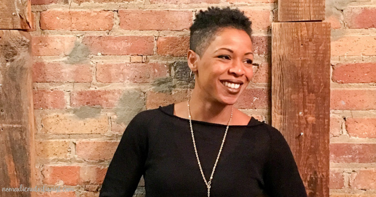 A headshot of a smiling black woman with short hair, a black shirt and gold hoop earrings.She is looking off to the right.