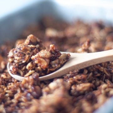 A spoon of kaniwa granola over a sheet pan of granola