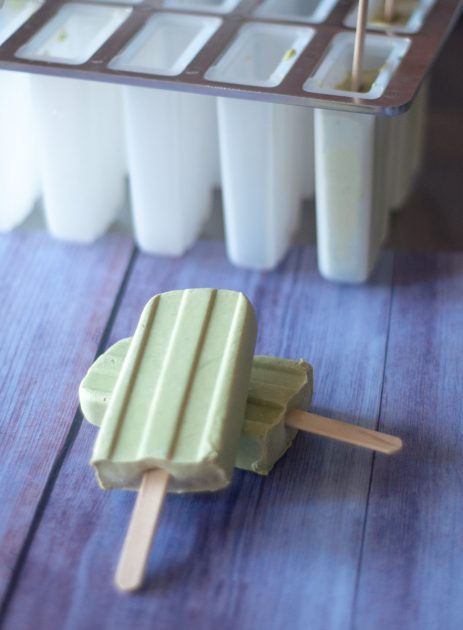Two avocado matcha popsicles on a purple board with a popsicle mold in the background