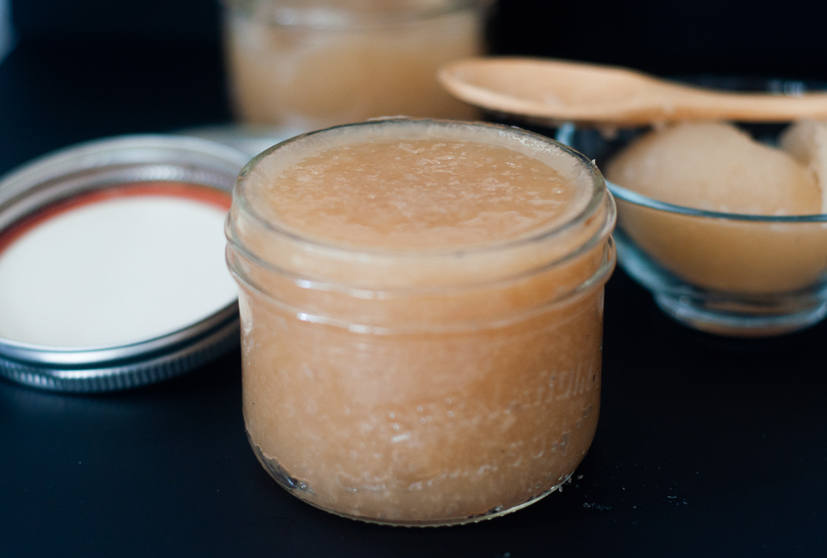 A close up of a small jar of Irish Moss Gel on a black table. A small bowl of gel and wooden spoon in the background.