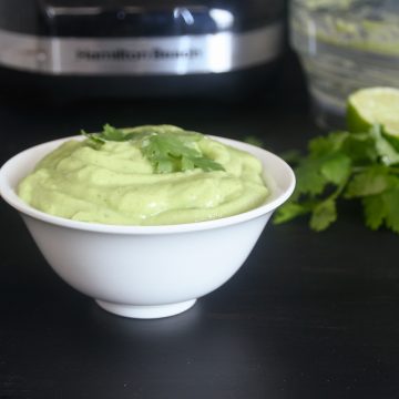 A small white bowl with light green avocado cilantro cream.