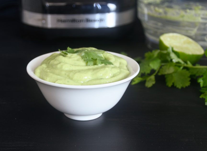 A small white bowl with light green avocado cilantro cream.