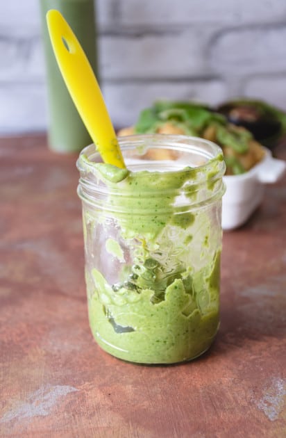 A small jar with a little bit of avocado cilantro cream left in the bottom. A yellow scoop is in the jar.