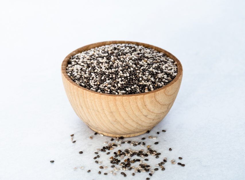Small wooden bowl of chia seeds with a few chai seeds spilling out onto the table.