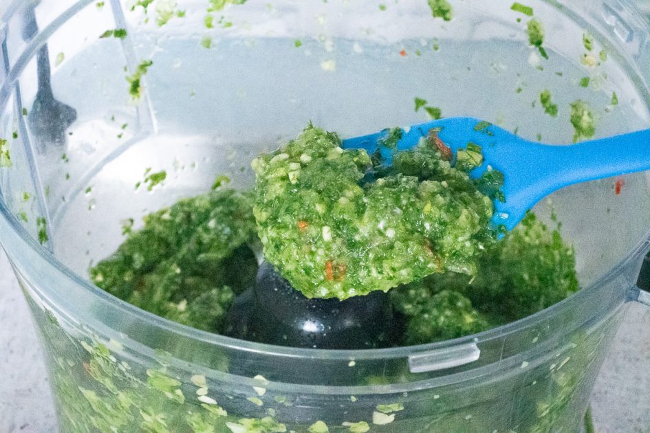 Scooping some green seasoning out of a food processor.