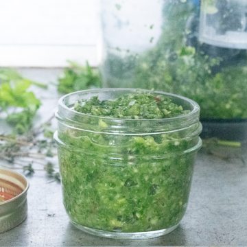 A small jar of green seasoning with a blender in the background