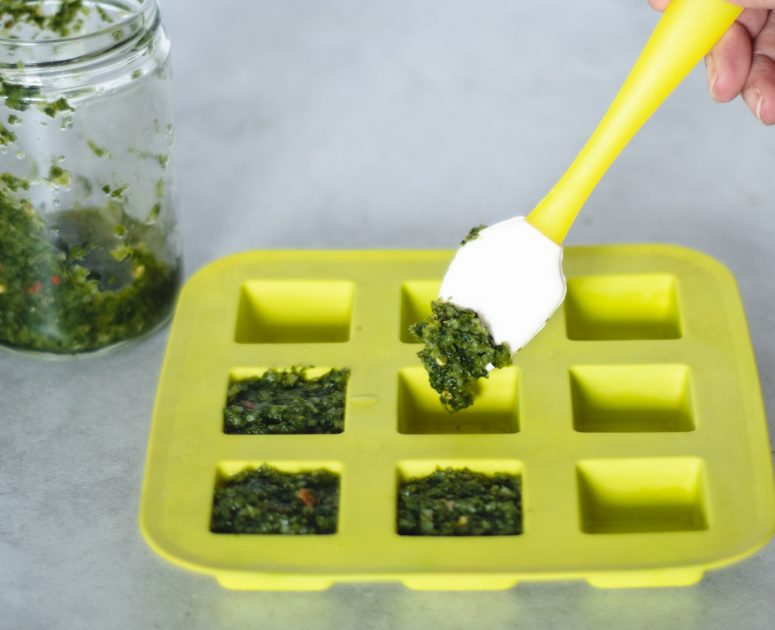 Putting freshly made green seasoning into a yellow silicone ice cube tray.