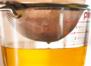 A large measuring cup with a wire mesh strainer, with ghee being strained through