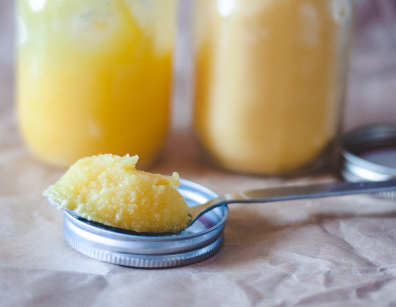 A teaspoon full of ghee, with two glass jars of ghee in the background