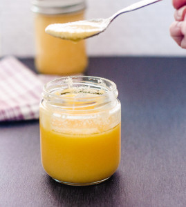 A small glass jar with freshly made ghee. A spoon holds some of the soft, slightly liquid ghee.