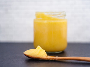 A small wooden spoonful of ghee with a small jar of ghee in the background