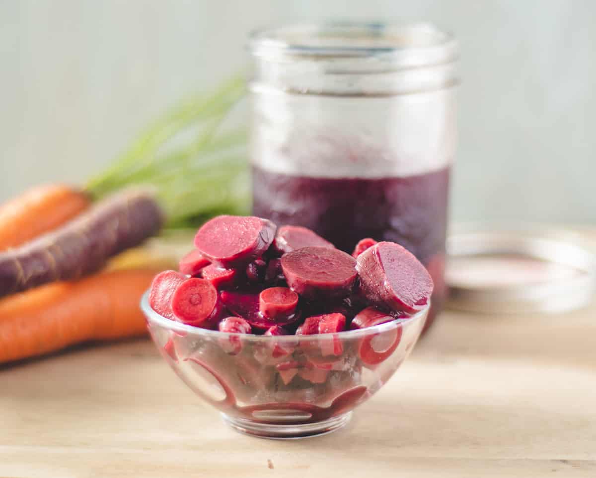 A small bowl of lactofermented carrots. Raw whole carrots in the background.