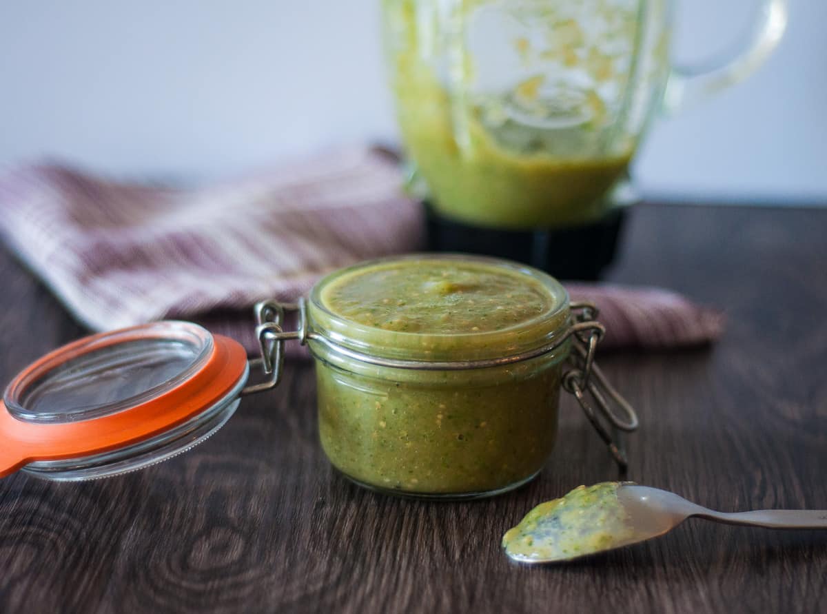 A small jar of roasted tomatillo salsa with a blender in the background