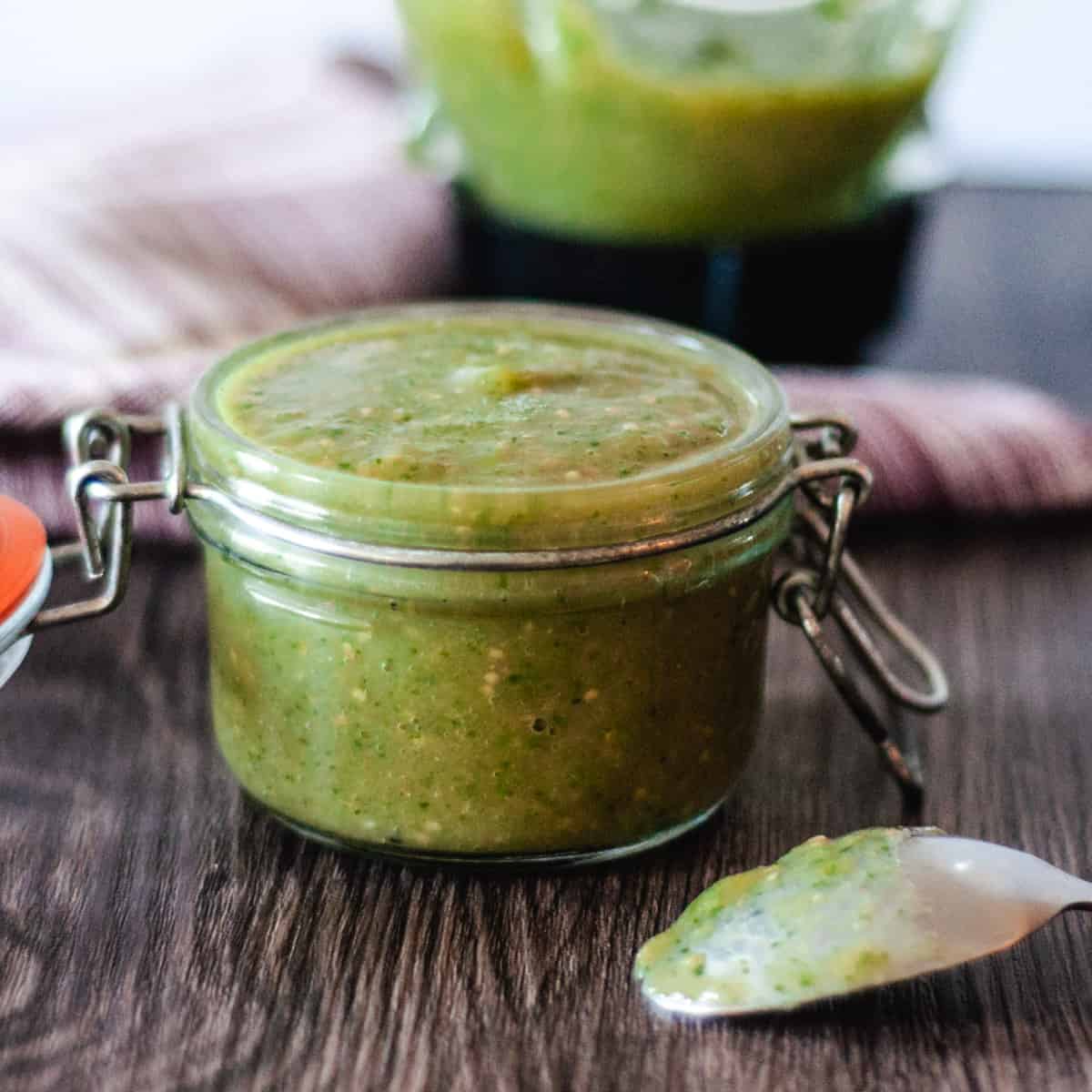 A small jar of roasted tomatillo salsa with a blender in the background