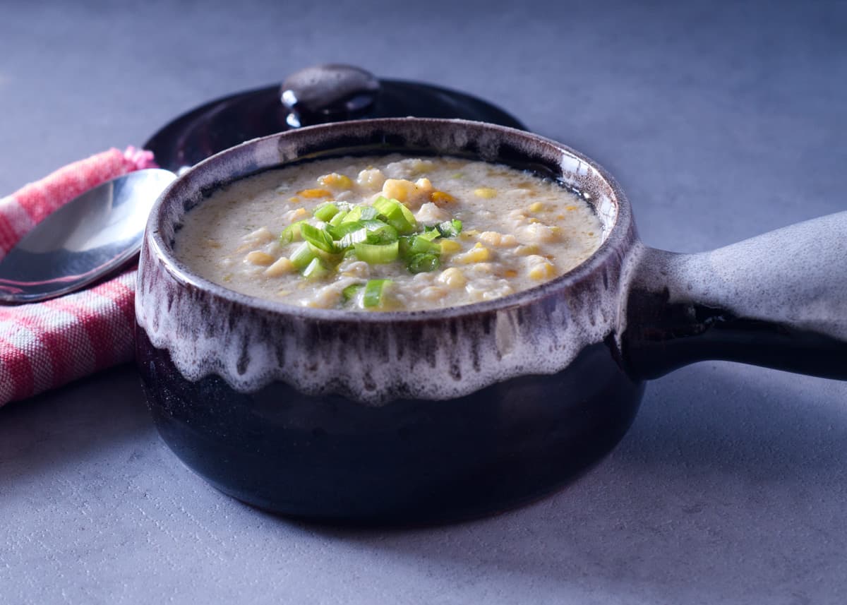 Chinese Trinidadian corn soup in a brown soup bowl topped with scallions