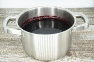 A small metal sauce pot on a wooden counter top with red sorrel inside.