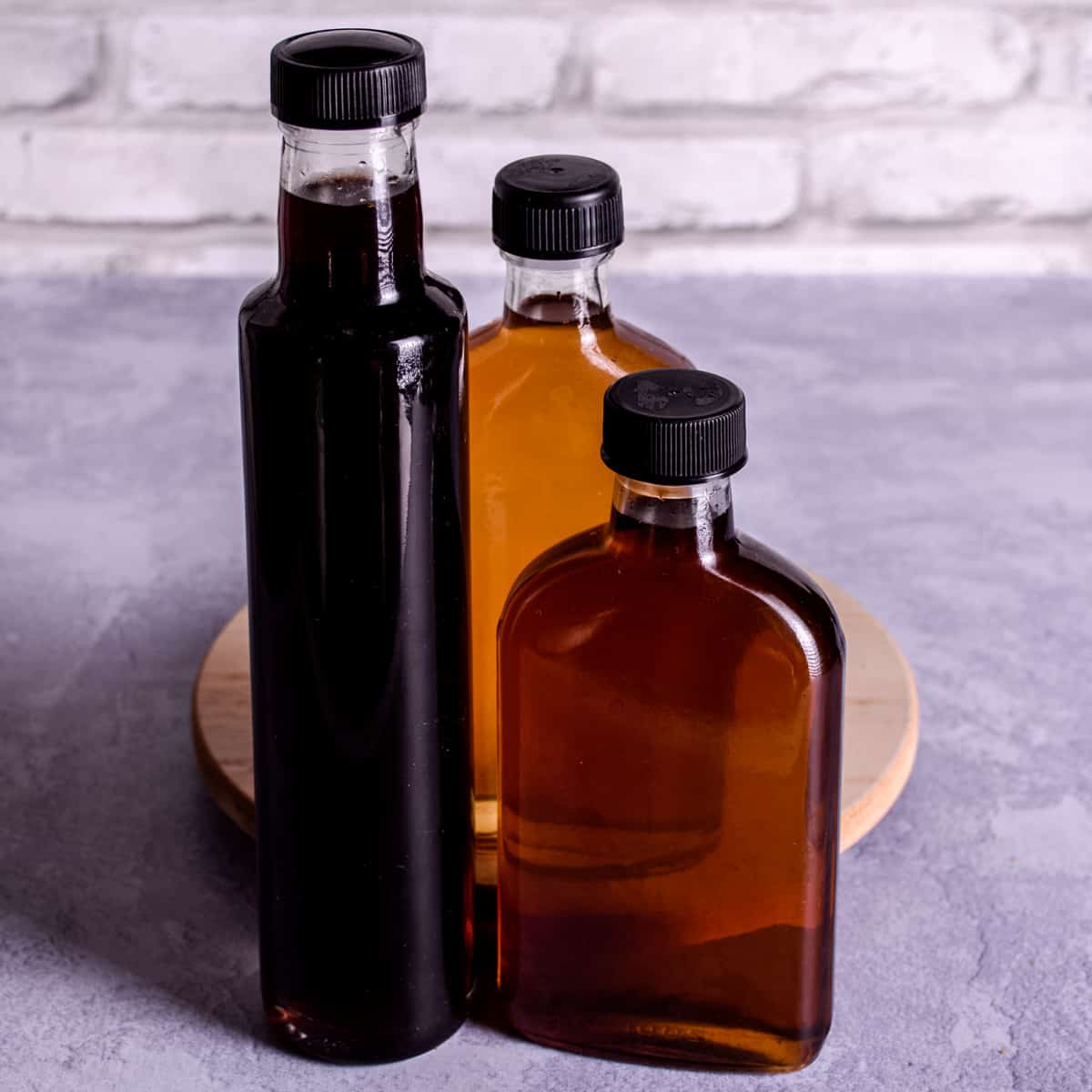 3 glass bottles of homemade simple syrup of varying colours: dark brown, amber and golden.