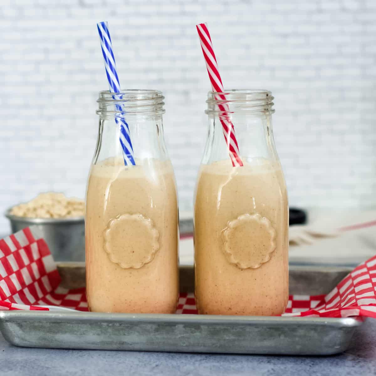 Two glass bottles filled with homemade peanut punch sit on a metal tray lined with red and white checked paper.