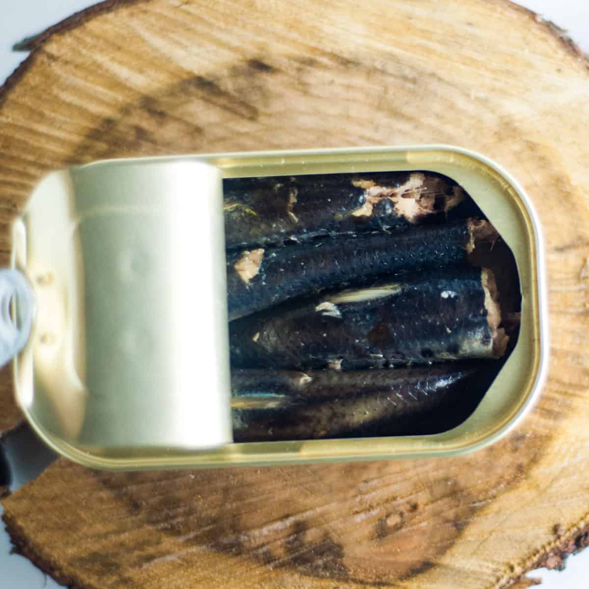 An open can of sardines on a wooden block