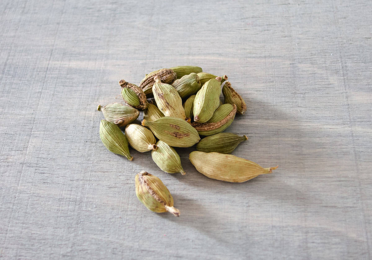 A small pile of green cardamom pods on a light grey surface.